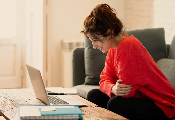 Squared images of woman working from home on ofa with laptop. On the table is books and pens and paper.